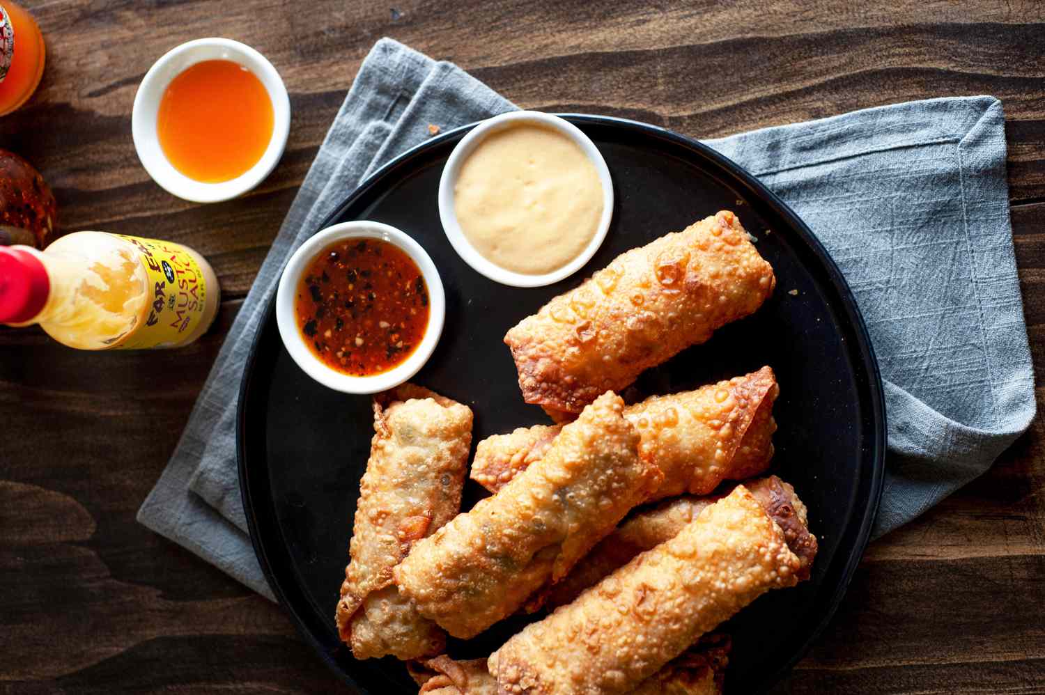 A dark plate with stacked vegetable egg rolls and dipping sauce