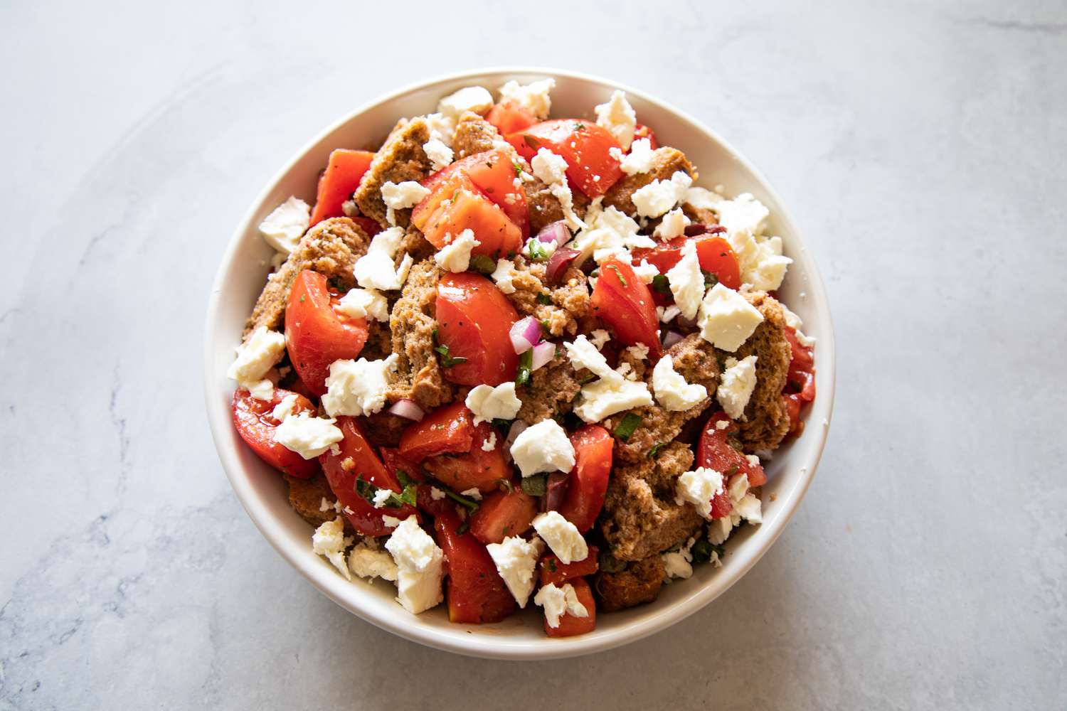 Feta added to a bowl along with tomatoes and bread for a summer vegetable salad with feta