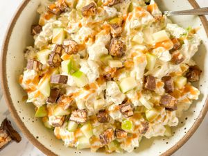 A bowl of Snickers salad with chopped apples, Snickers pieces, and caramel drizzle, served in a ceramic dish