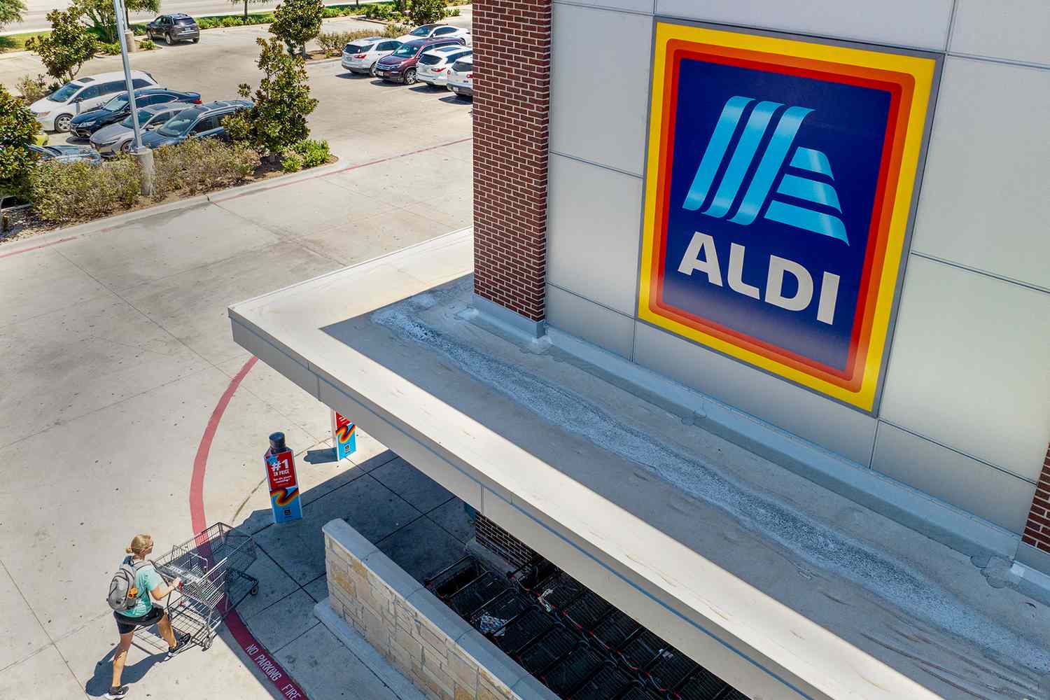 An Aldi store entrance with a shopper pushing a cart toward it