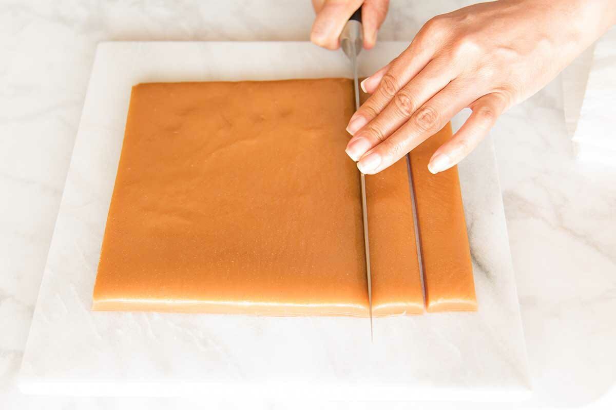 How to make soft and chewy caramels with a person using a knife to cut the square of caramel vertically.