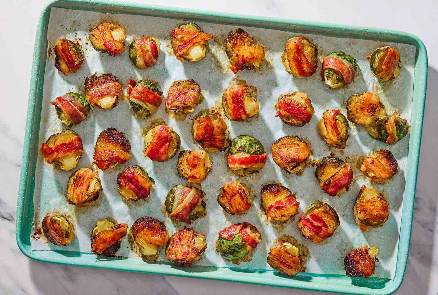 Bacon wrapped Brussels sprouts on a light blue baking sheet