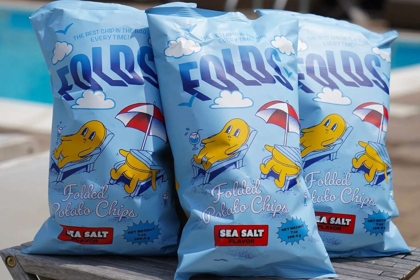 Three bags of Folds folded potato chips sea salt flavor on a wooden surface outdoors