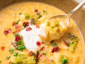 A spoonful of broccoli potato soup garnished with scallions bacon and cream