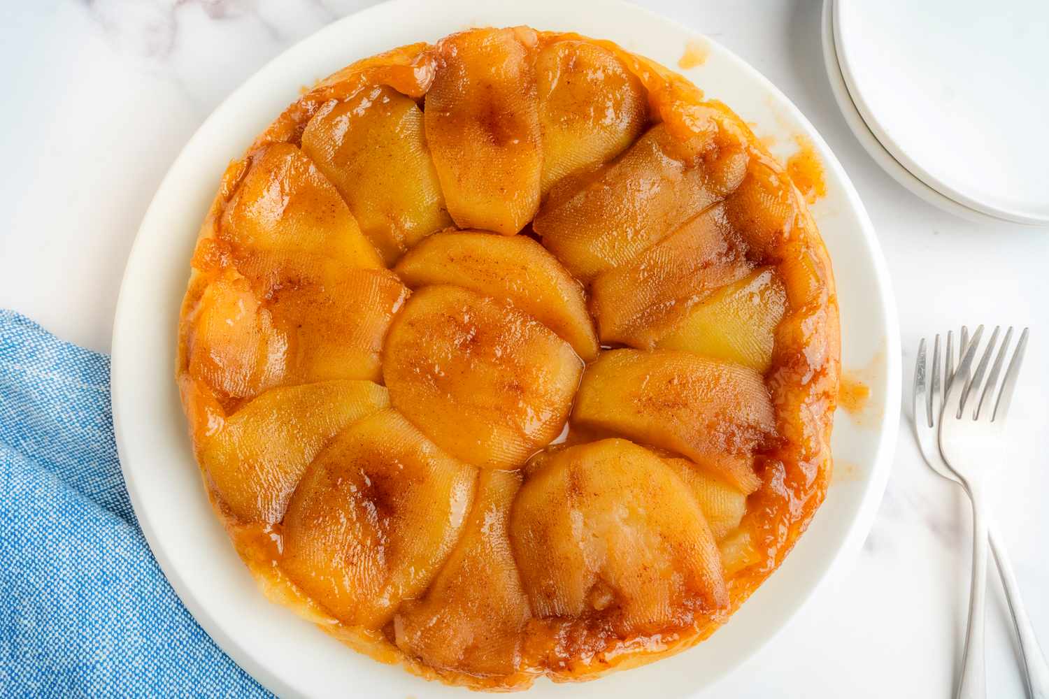 A tarte tatin placed on a white plate a dessert consisting of caramelized fruit arranged over a pastry base