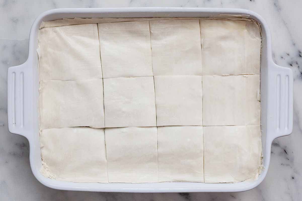 Phyllo cut into squares lining the top of of a casserole dish filled with spinach and cheese for spanakopita.