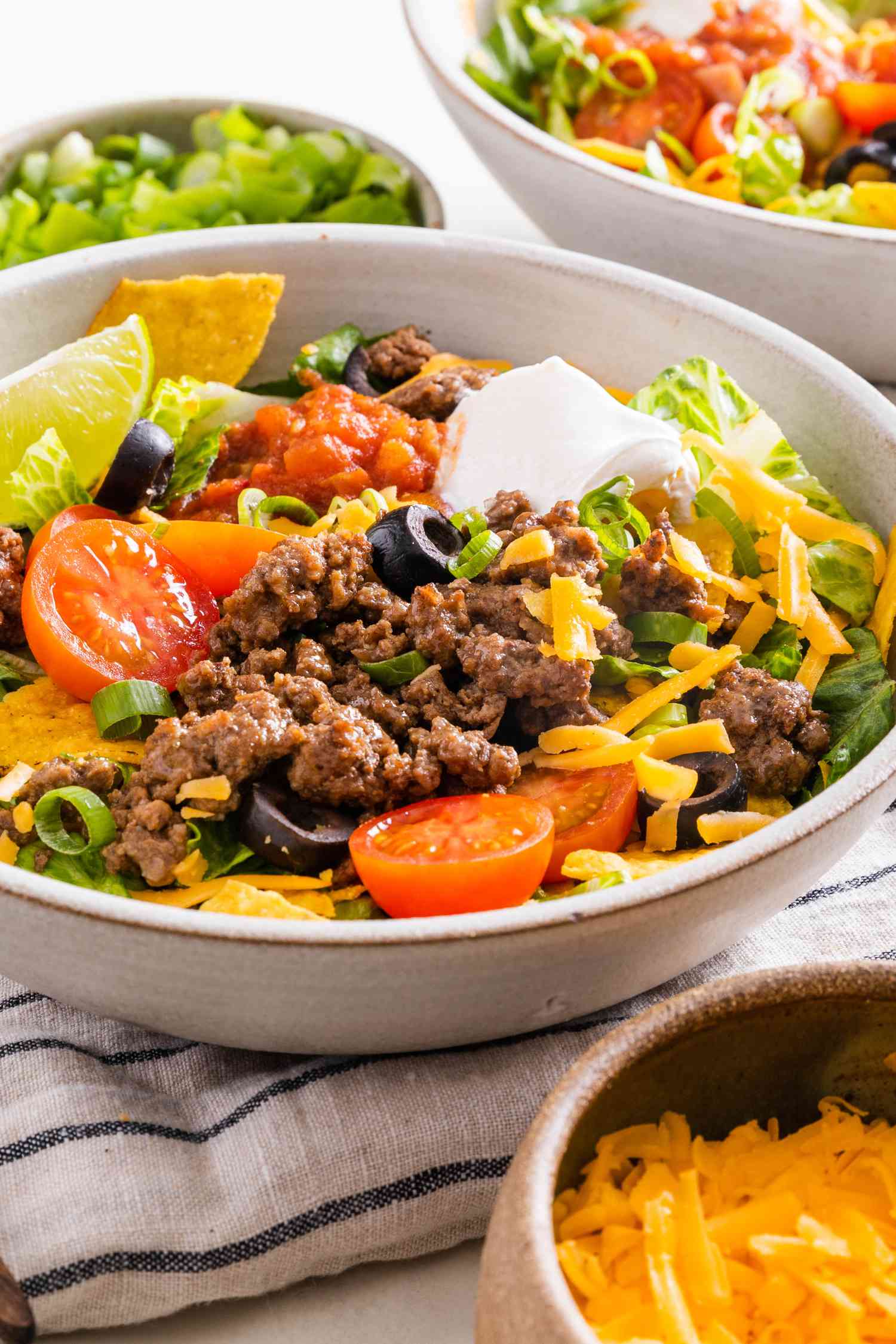 Taco Salad in a Bowl, and in the Surroundings, Another Serving in a Bowl, a Bowl of Sliced Scallions, and a Bowl of Cheese