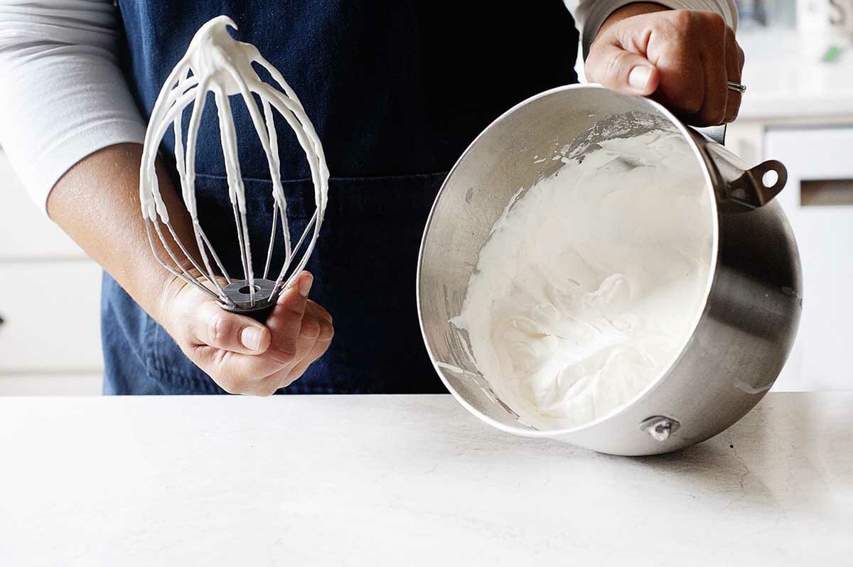 A person tipping the metal bowl of a stand mixer to show the whipped cream inside.