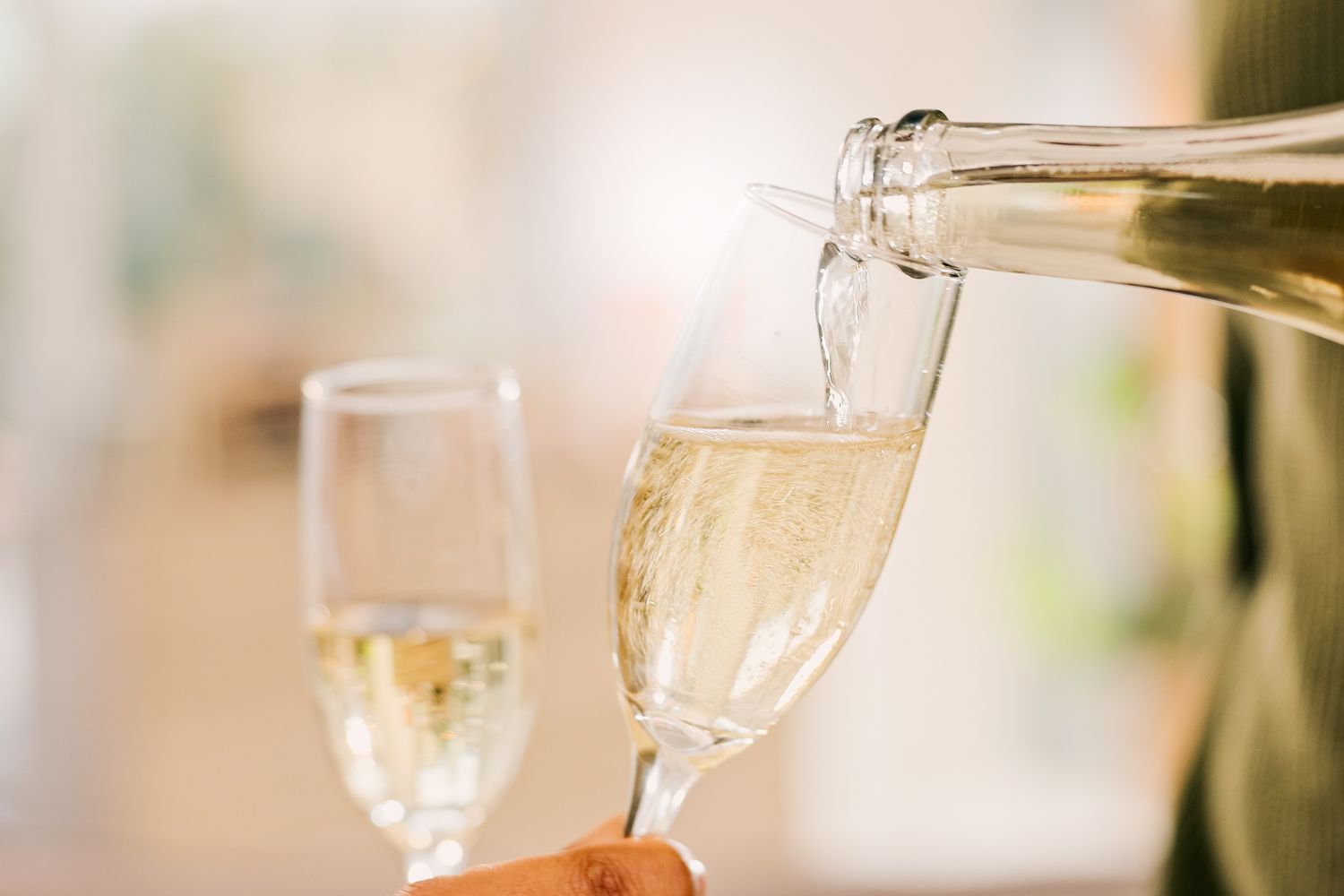 Pouring sparkling wine into a glass with another filled glass in the background