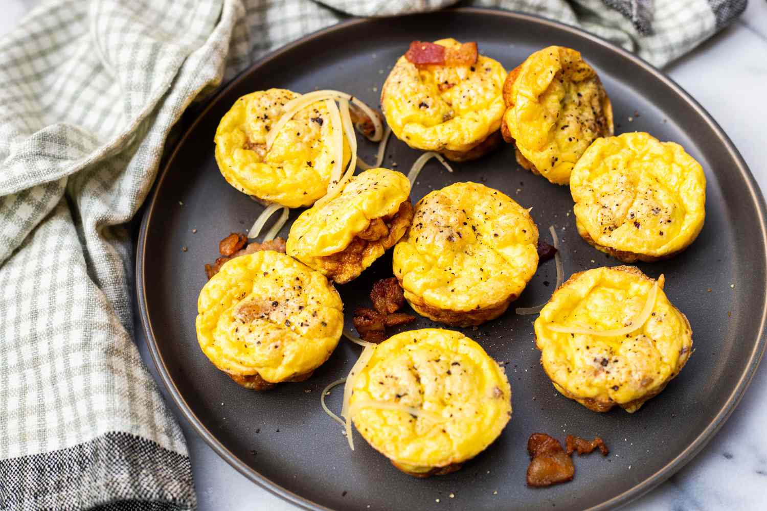 Bacon and Gruyère Egg Bites on a Plate Topped with Shredded Cheese, Bacon, and Cracked Pepper