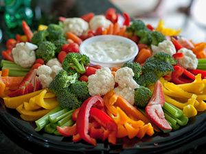 A vegetable tray with celery bell peppers broccoli cauliflower and dip in the center
