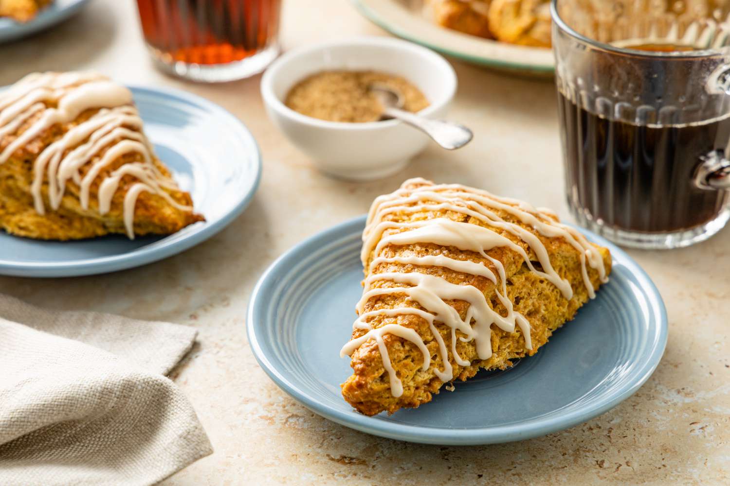 Pumpkin Scones on Plate Surrounded by Cups of Coffee and a Bowl of Sugar