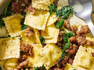 Closeup view of ravioli, Italian sausage and spinach topped with Parmesan cheese in a bowl with a spoon