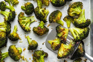 Roasted broccoli on a baking sheet with a spatula scooping some pieces