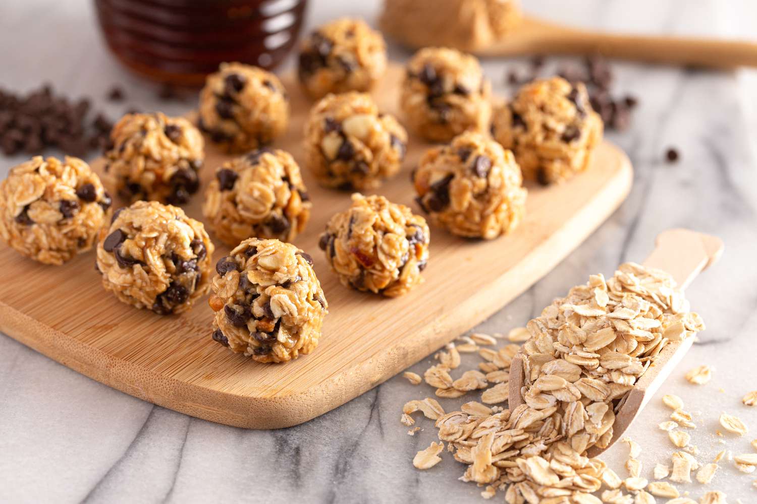 Chocolate oat balls on a wooden board next to a scoopful of oats on the counter