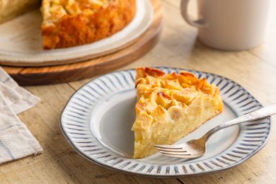 slice of Easy French Apple Cake on a dessert plate with a fork in the forground, cake on a serving board
