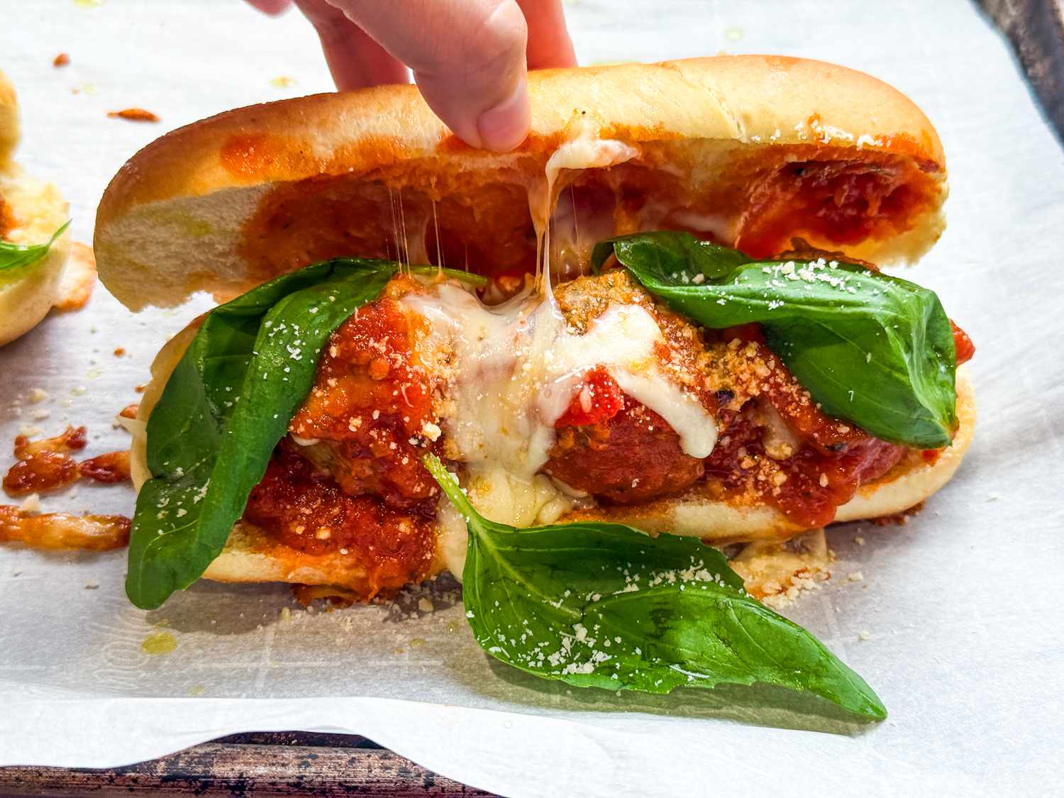A meatball sub with basil, showing a cheese pull