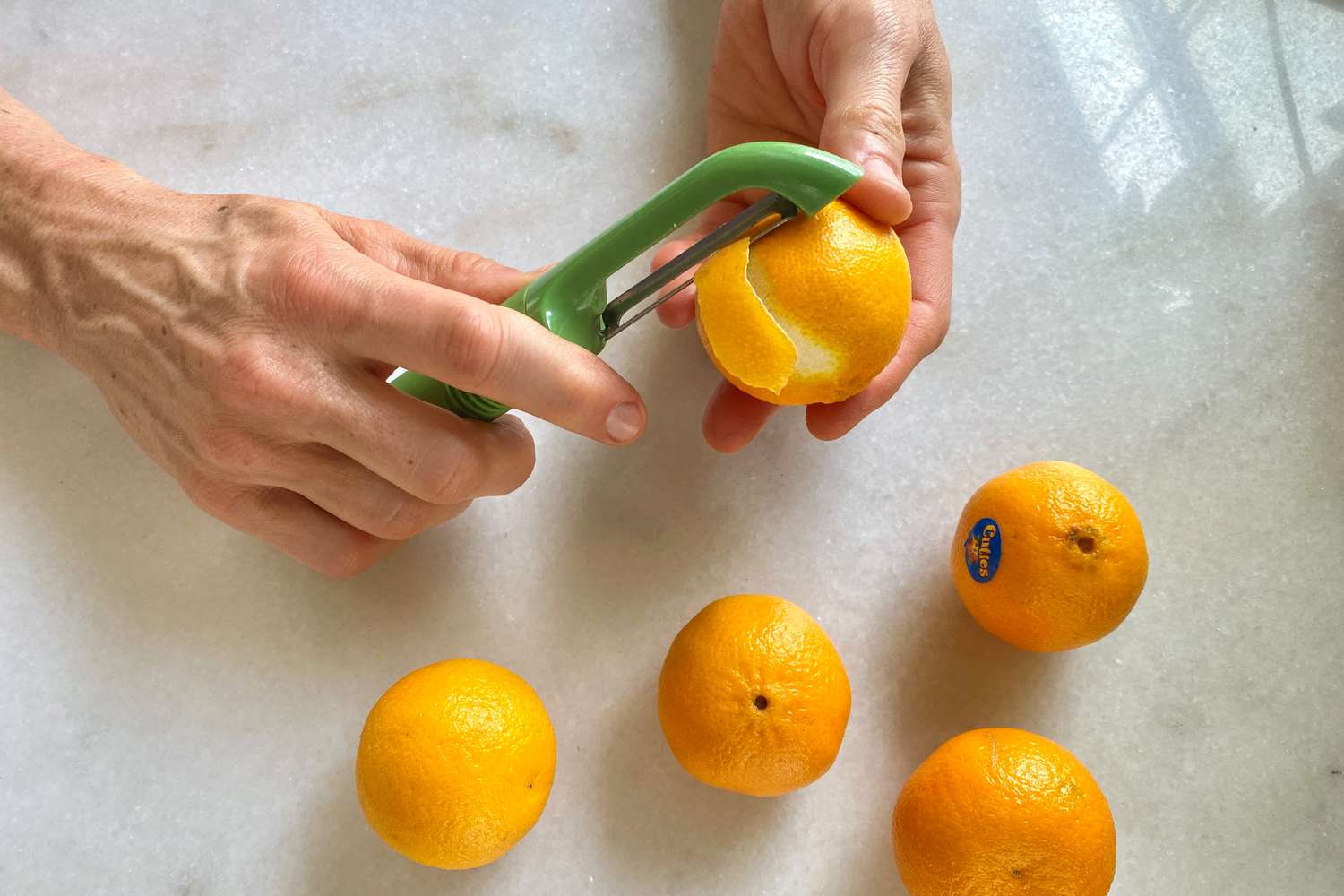 Hands peeling a clementine with a vegetable peeler