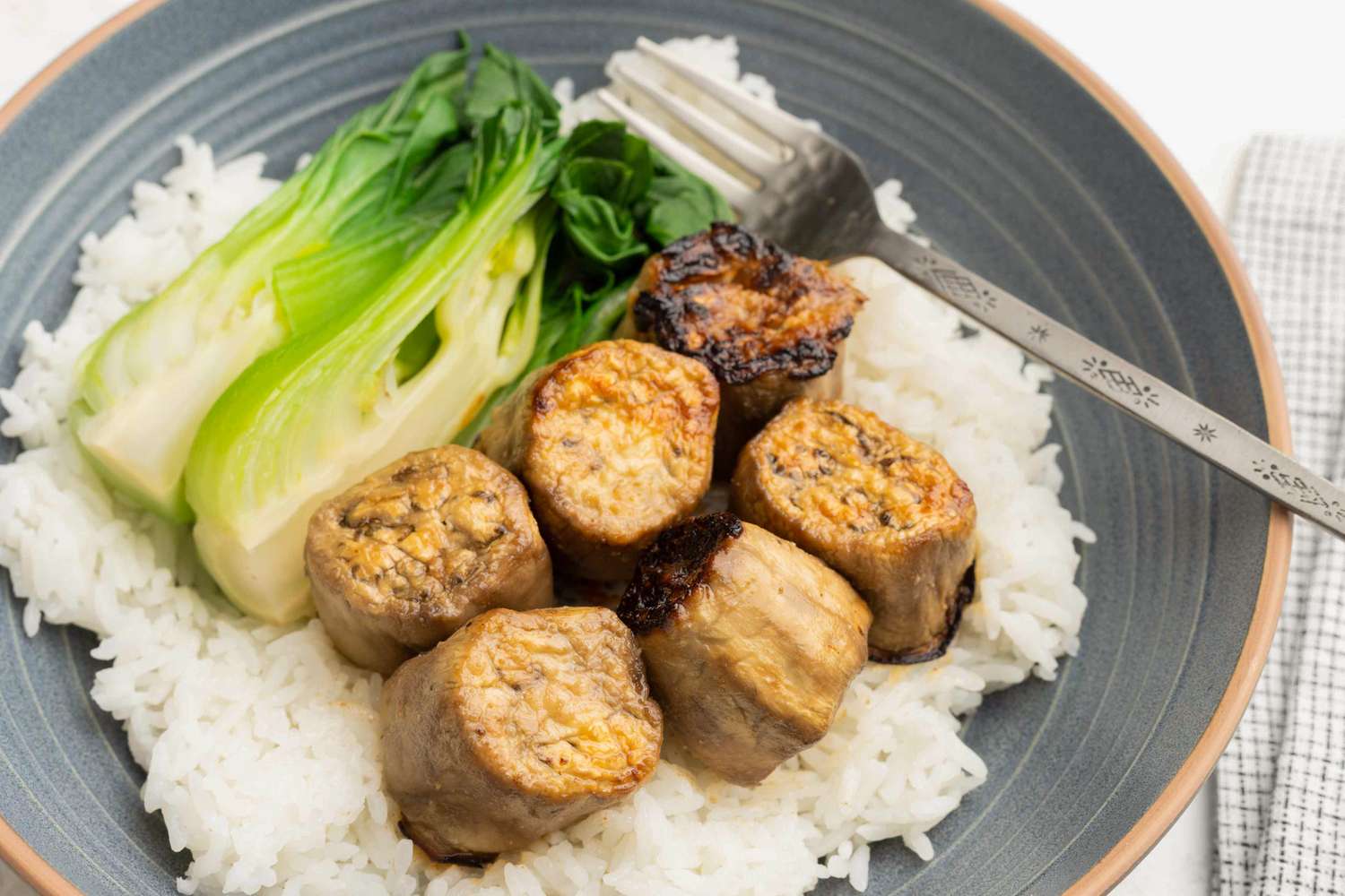 Miso-Glazed Eggplant on a bed of rice with baby bok choy on a plate with a fork