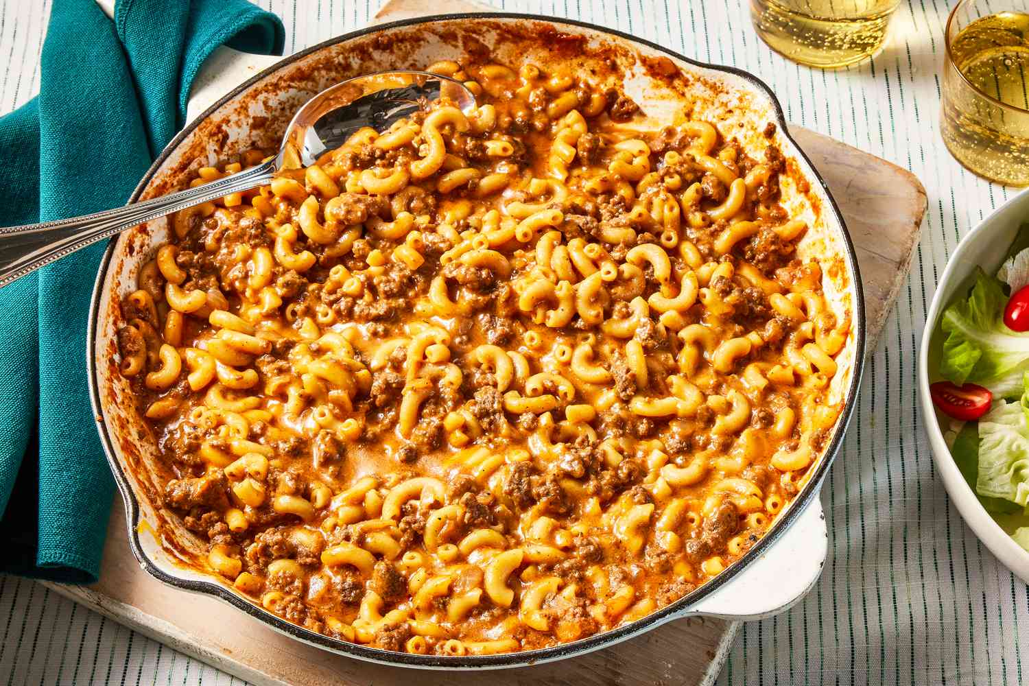 homemade hamburger helper in a skillet at a table setting with two glasses of soda and a side salad