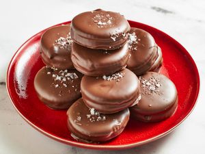 Stack of chocolate coated ritz crackers on a red plate sprinkled with a topping