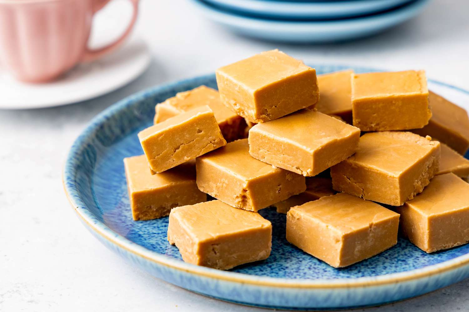 Penuche on a plate, and in the background, a teacup and a stack of plates