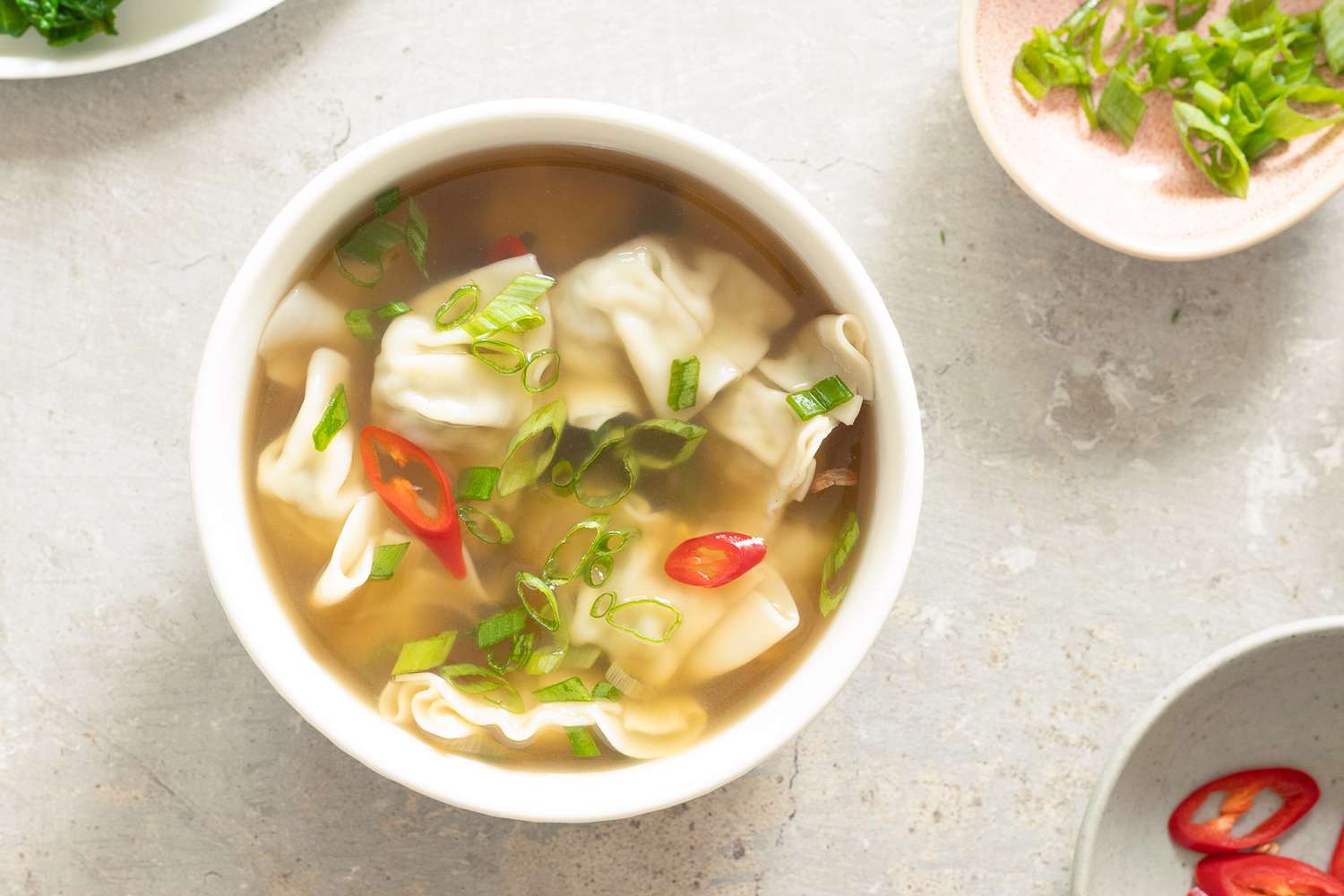wanton soup next to a small bowl of sliced scallions