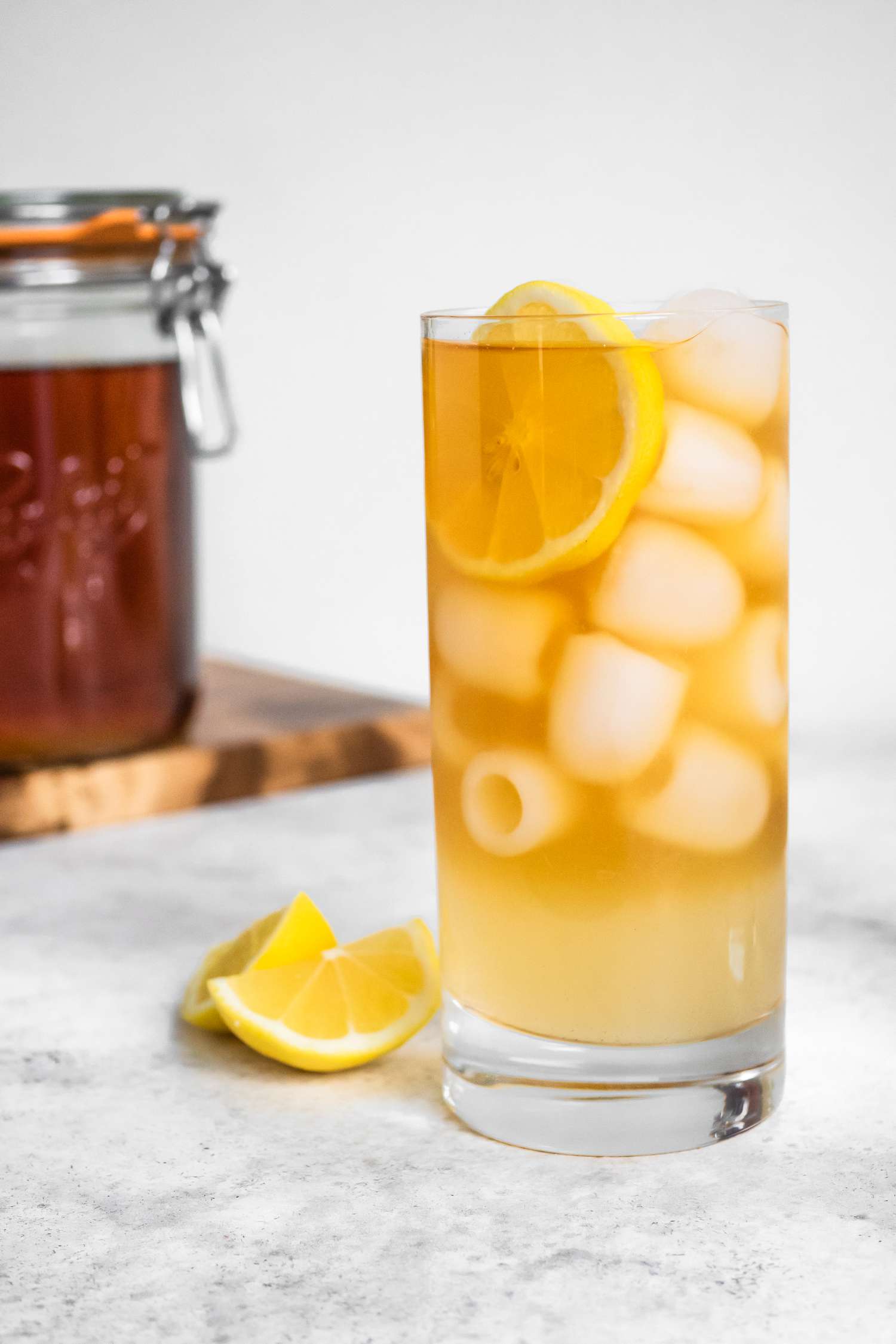 Glass of Arnold Palmer With a Lemon Slice, Next to a Jar of Black Tea on a Wooden Board and Two Lemon Wedges