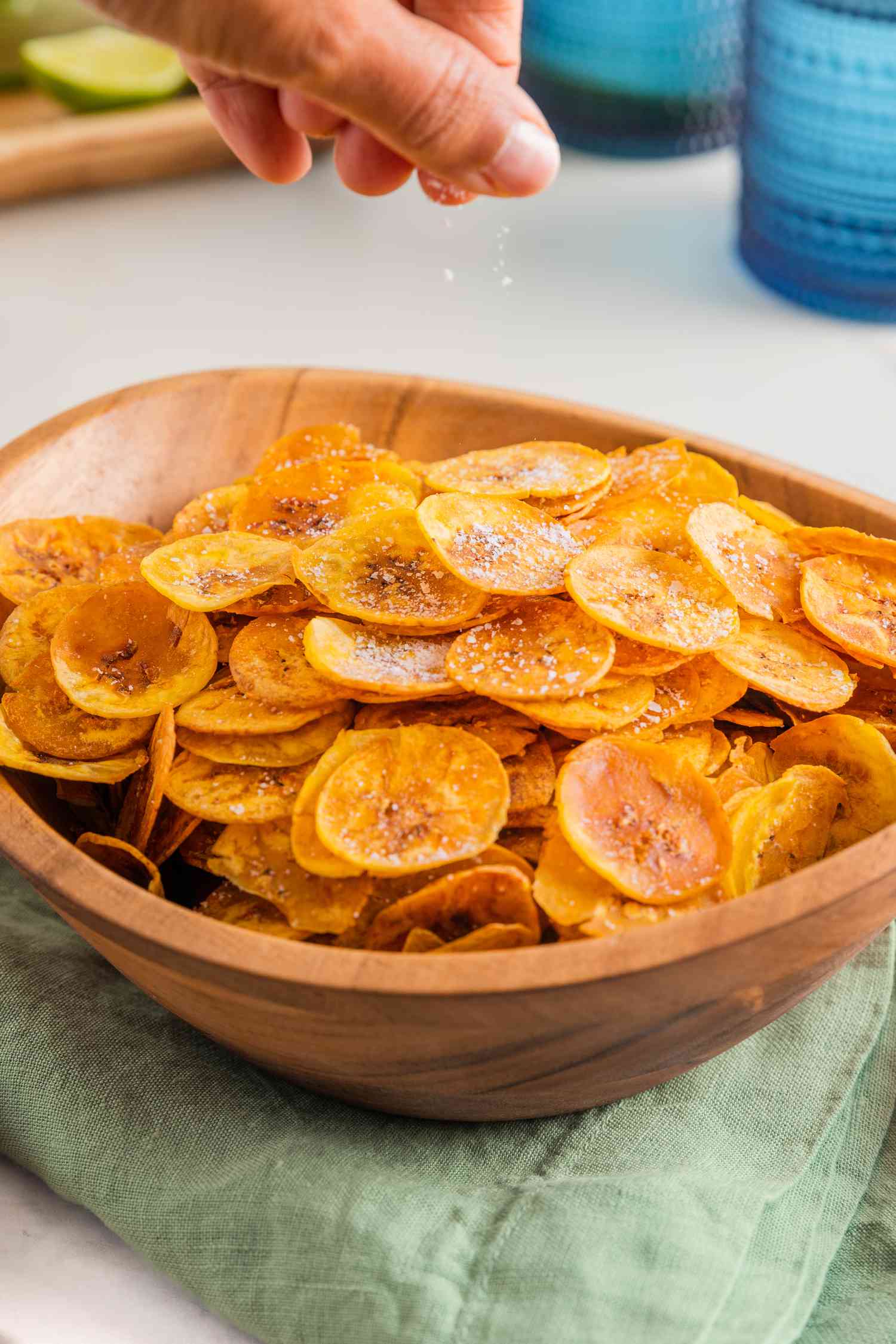 Hand Sprinkling Salt on Plantain Chips in a Large Bowl