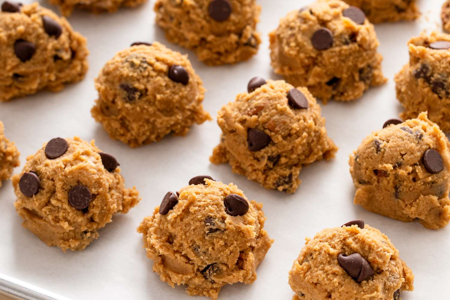 Dough balls with chocolate chips arranged on a baking parchment