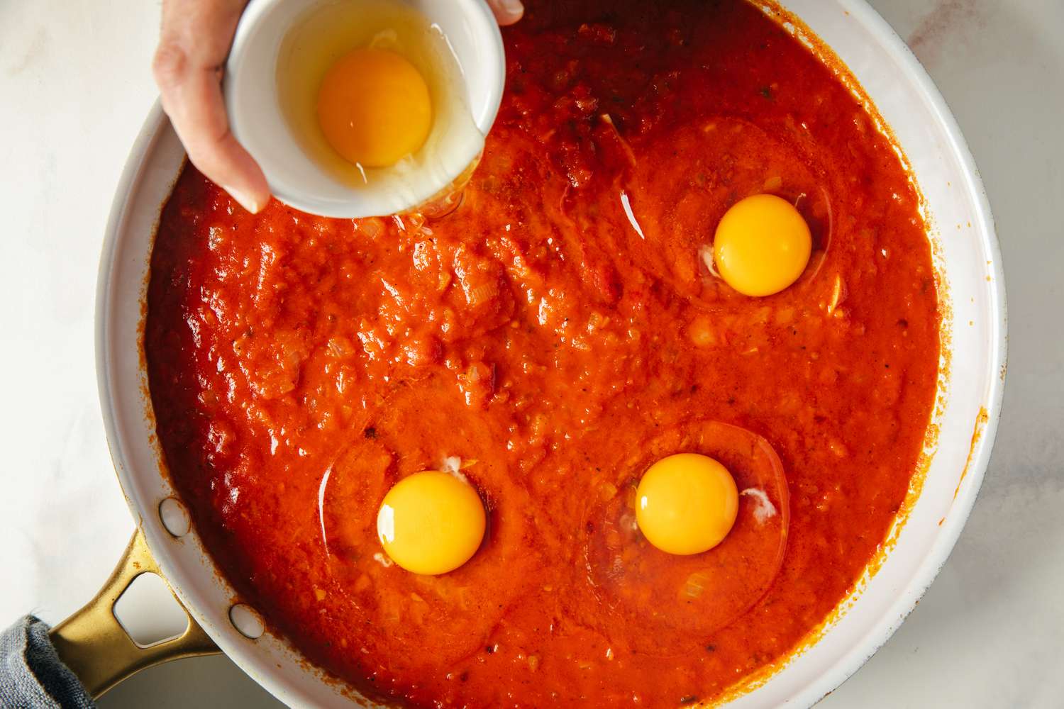 Eggs being added to a skillet with tomato sauce an overhead view showcasing the cooking process of eggs in purgatory