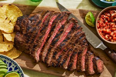 Sliced carne asada fanned out on a cutting board with salsa and tortillas nearby