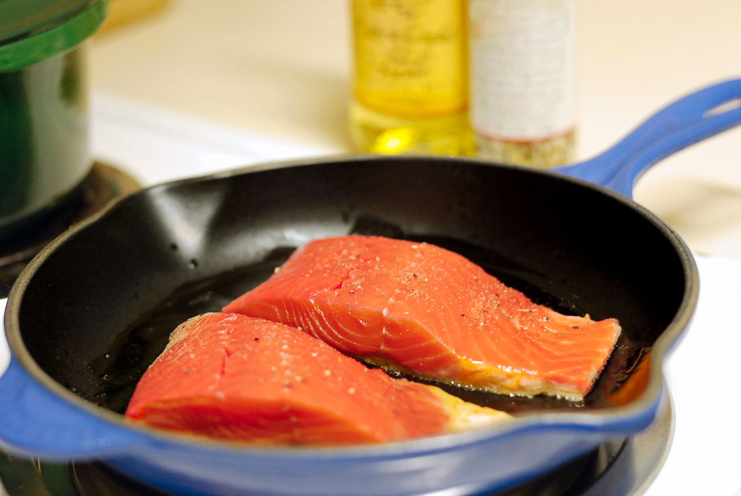 Two salmon fillets cooking in a blue skillet