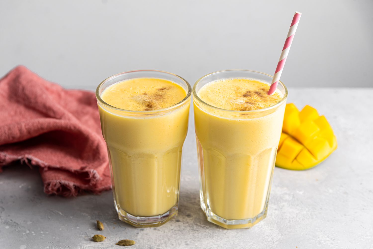 Two Mango Lassi Drinks in Glasses, One With a Straw