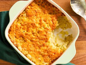 Overhead view of a square white baking dish of potato cabbage casserole sitting on a dark green napkin next to a serving spoon all on a wooden tabletop