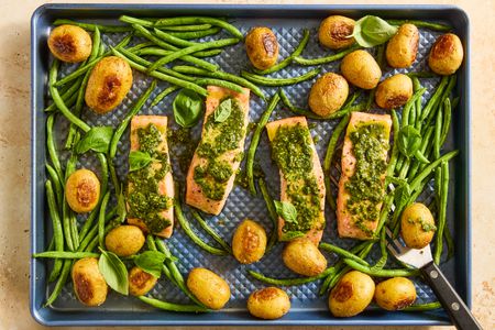 A sheetpan with salmon fillets topped with pesto, green beans, potatoes and basil