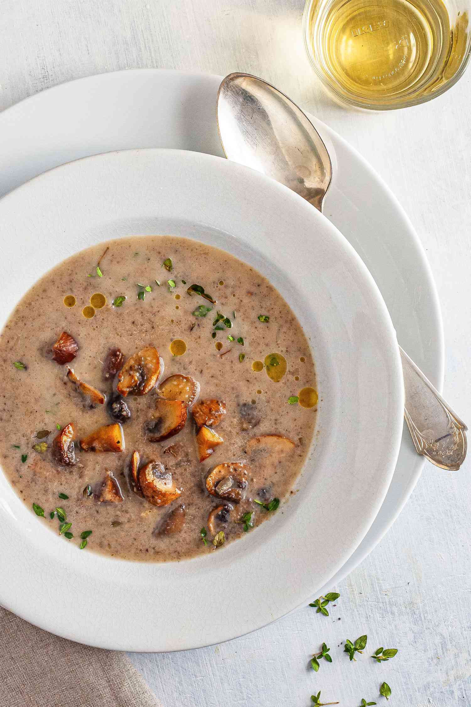 Chestnut mushroom soup in a white bowl with a white plate underneath.