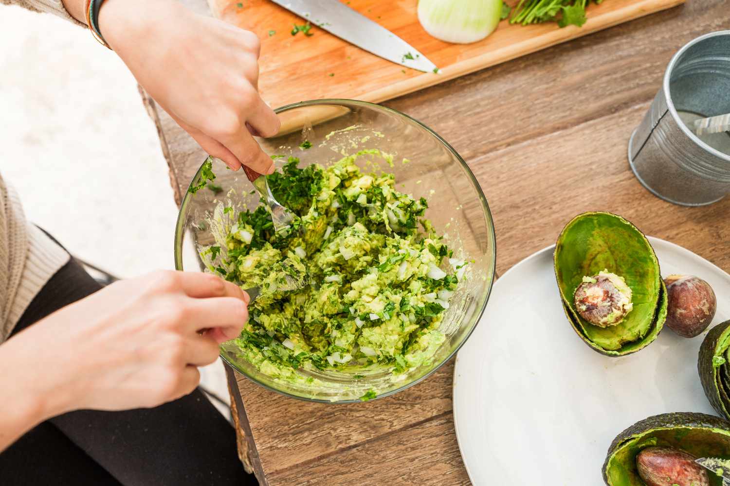 Overhead view of a woman mixing ingredients in a glass bowl for a guacamole recipe