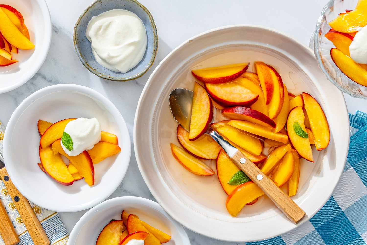 Bowls of sliced fruit served with a creamy topping and garnished with a mint leaf, displayed on a table with utensils