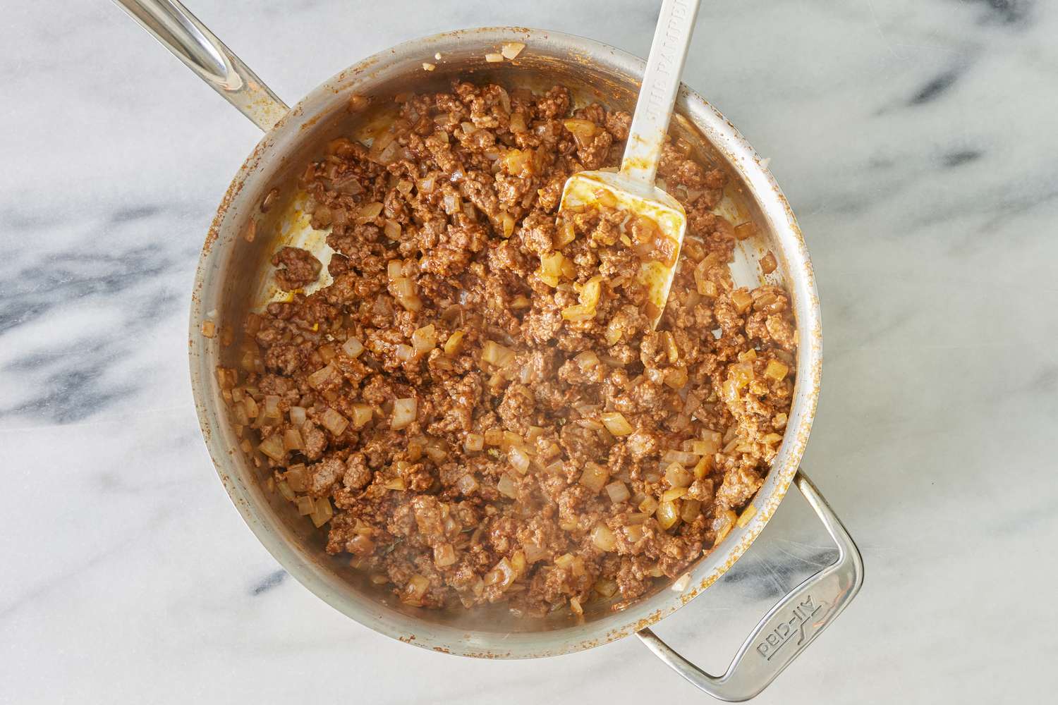 ground beef stirred into the cooked onions in the pot for cowboy casserole recipe