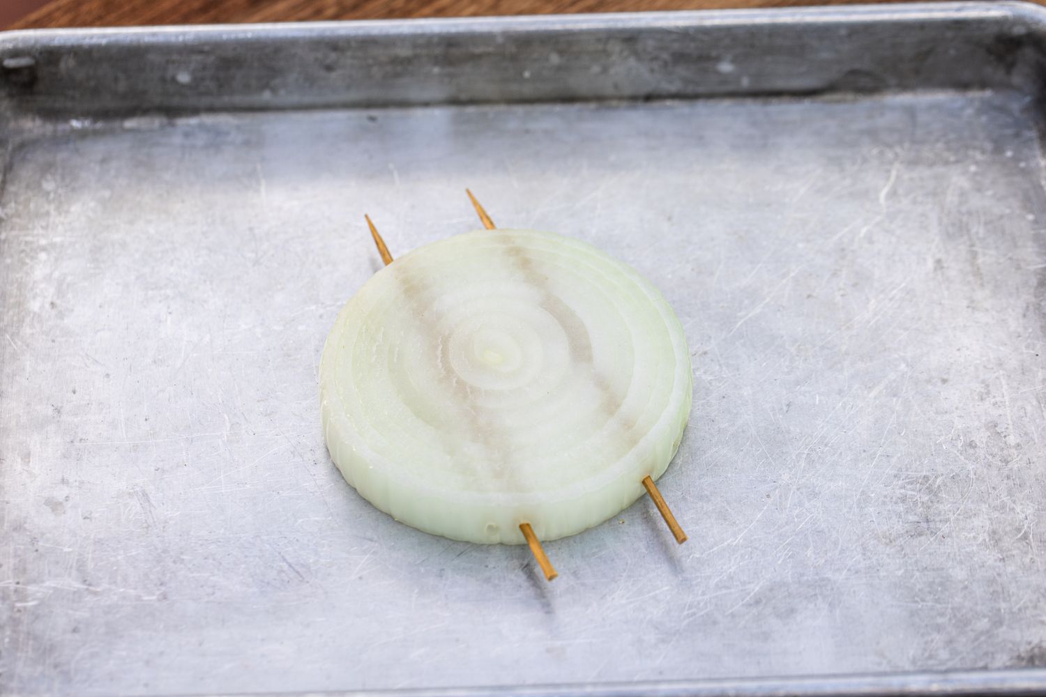 Skewered sliced onions on a baking sheet for a grilled onions recipe.