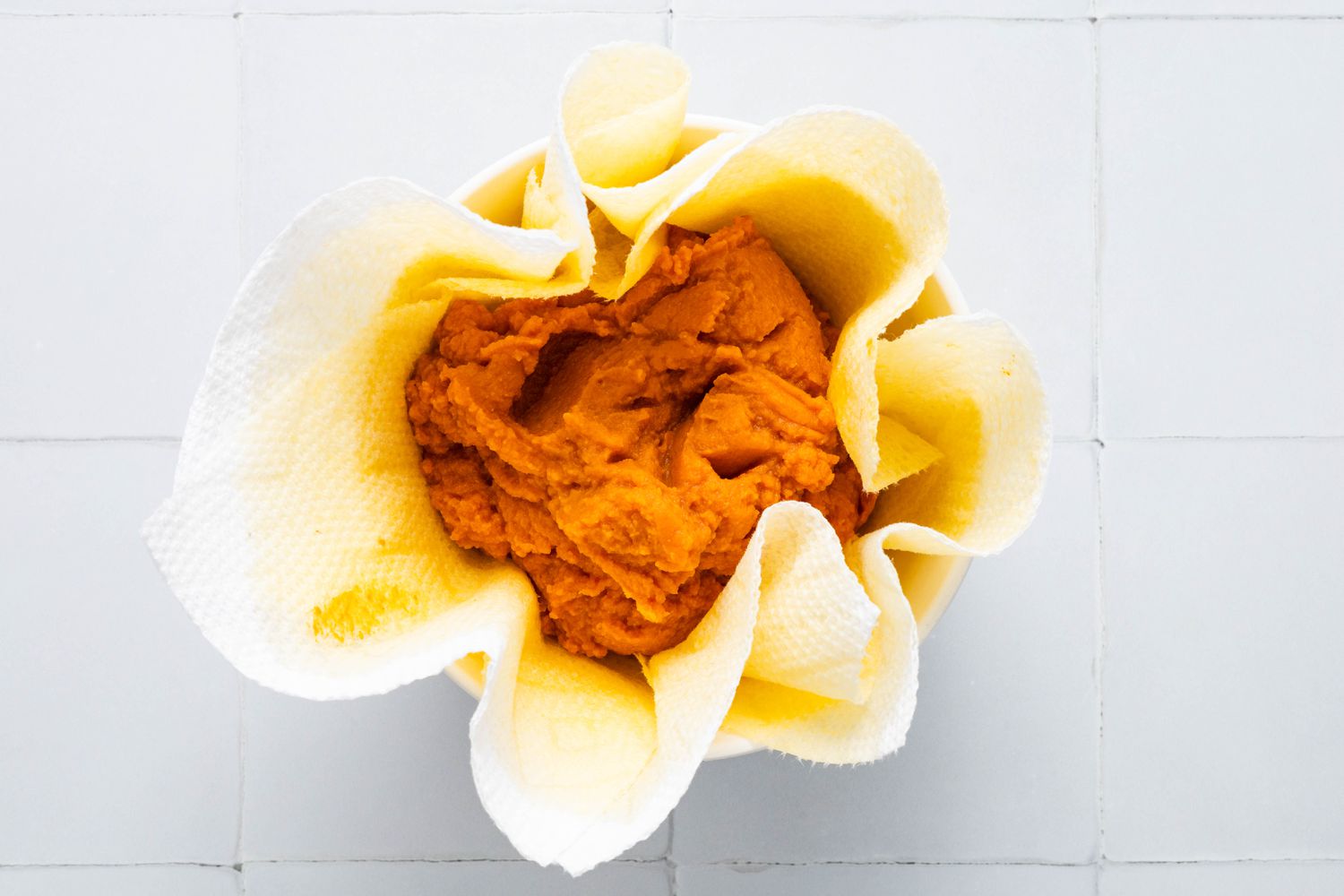 Pumpkin puree in a paper towel lined bowl for Cookie crumb, butter, and sugar blended together in a food processor for no-bake pumpkin cheesecake recipe