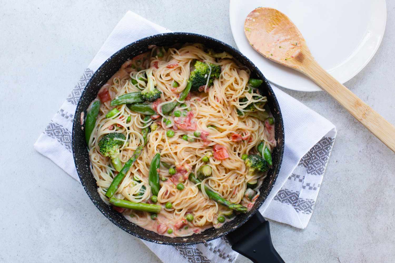 Overhead view of pasta primavera in a skillet with a wooden spoon next to it.