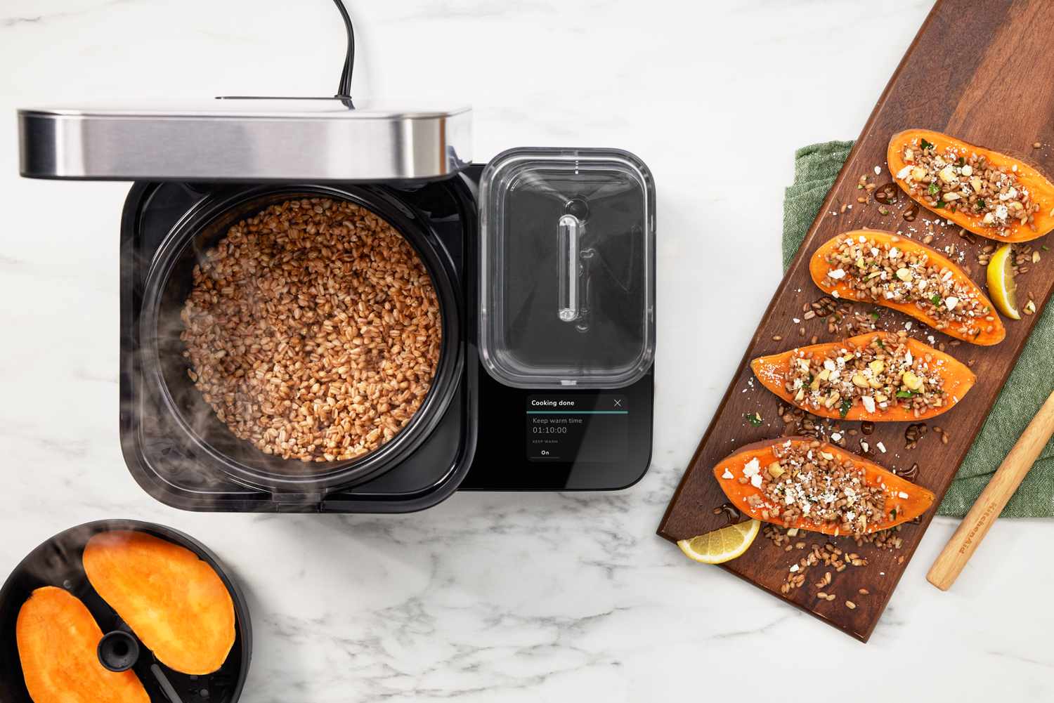 An overhead shot of the KitchenAid rice cooker with the lid open showing cooked farro, next to four sweet potato halves topped with farro and crumbled feta.