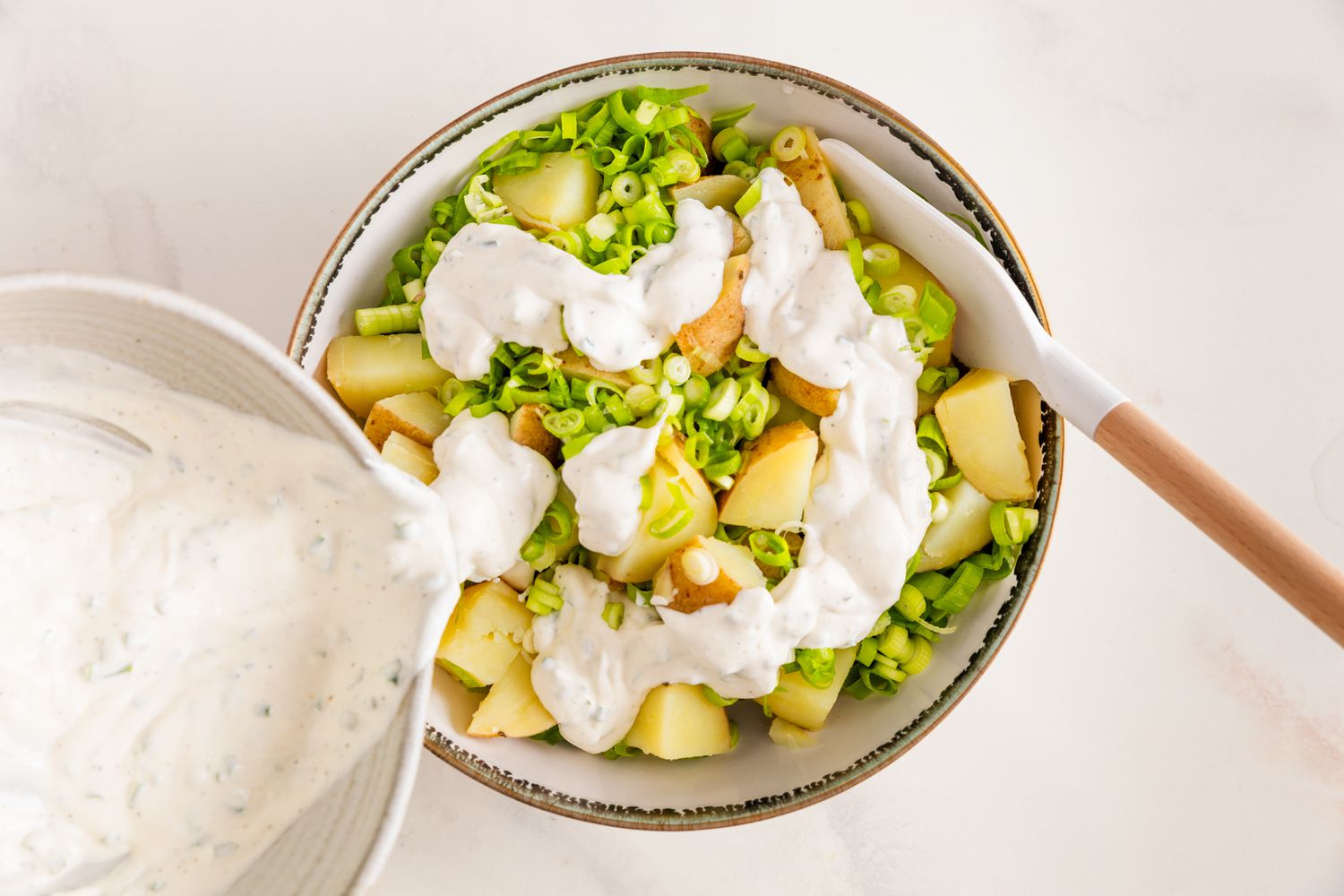 Sour Cream and Onion Dressing Poured Onto the Potatoes and Green Onion Slices in a Bowl With a Rubber Spatula