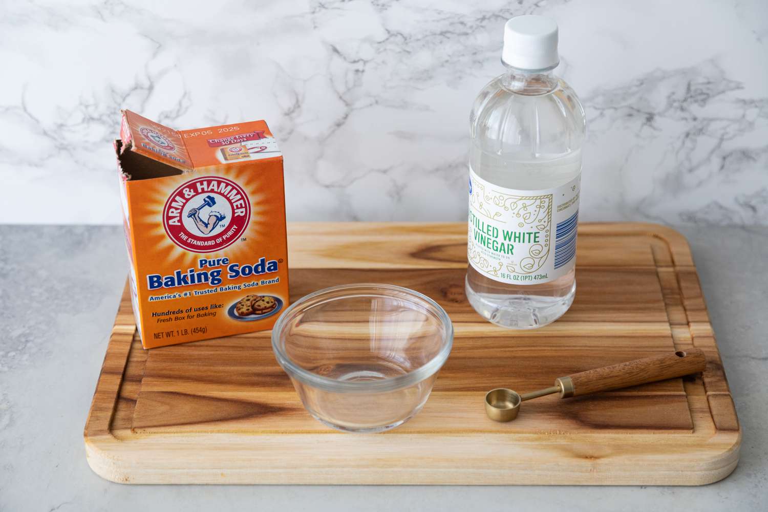 Box of Baking Soda, a Bottle of White Vinegar, a Measuring Spoon, and a Small Bowl on a Cutting Board 
