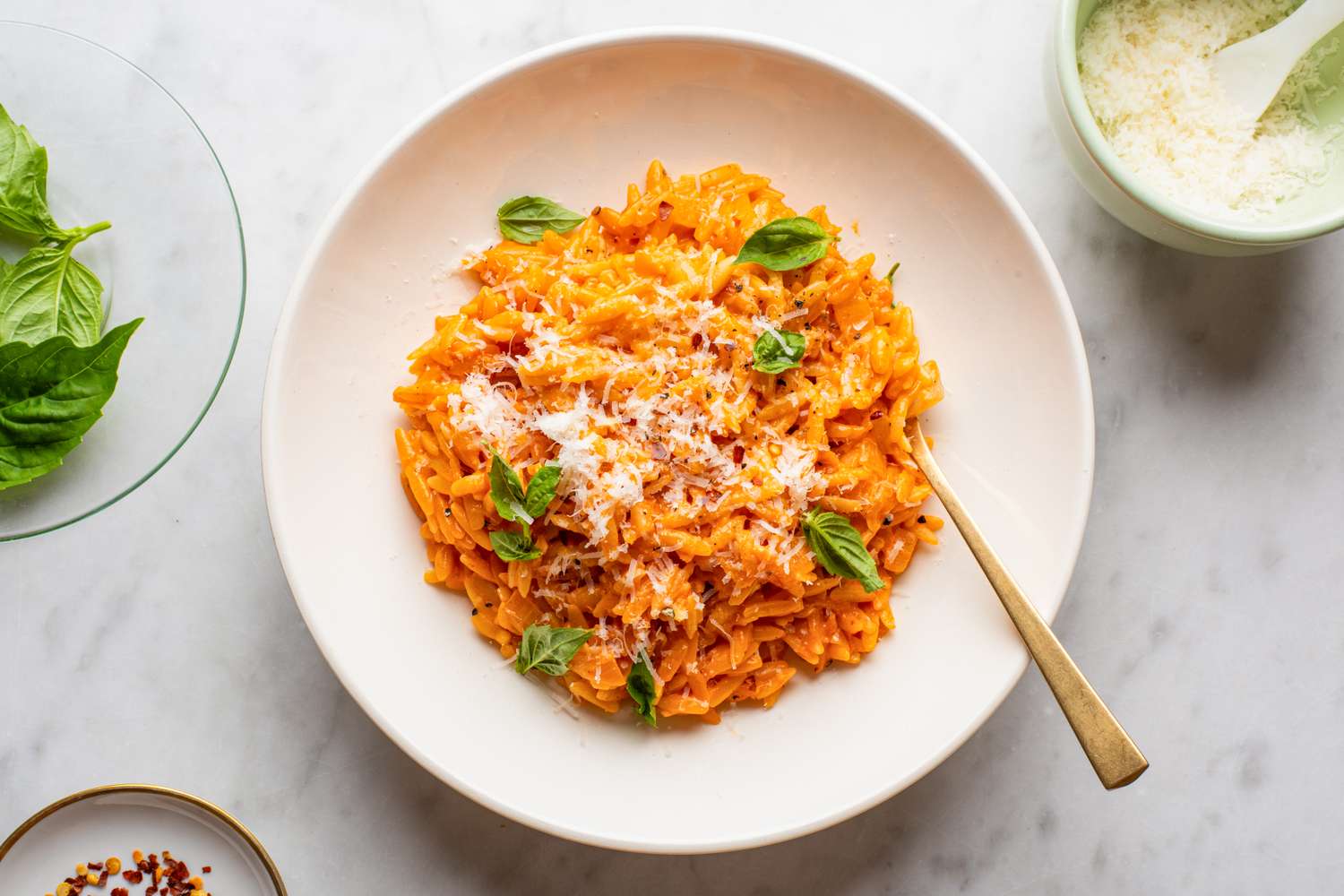 Orzo in vodka sauce garnished with grated cheese and fresh basil served in a white bowl with a gold spoon