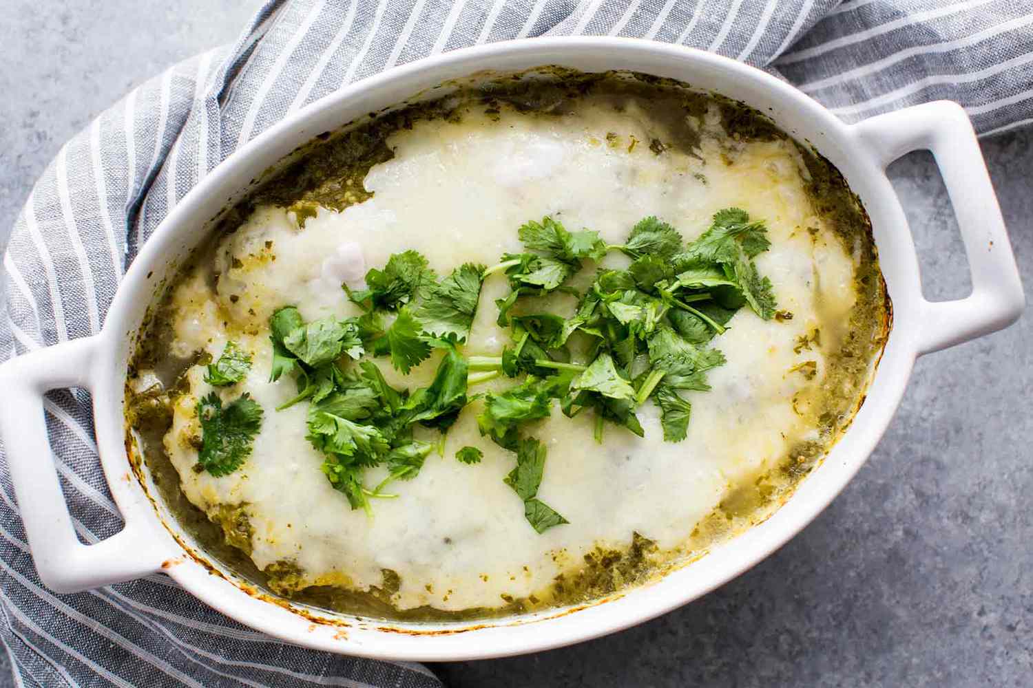 a dutch oven of salsa verde chicken bake with cilantro on top sits ready to serve on a gray kitchen towel