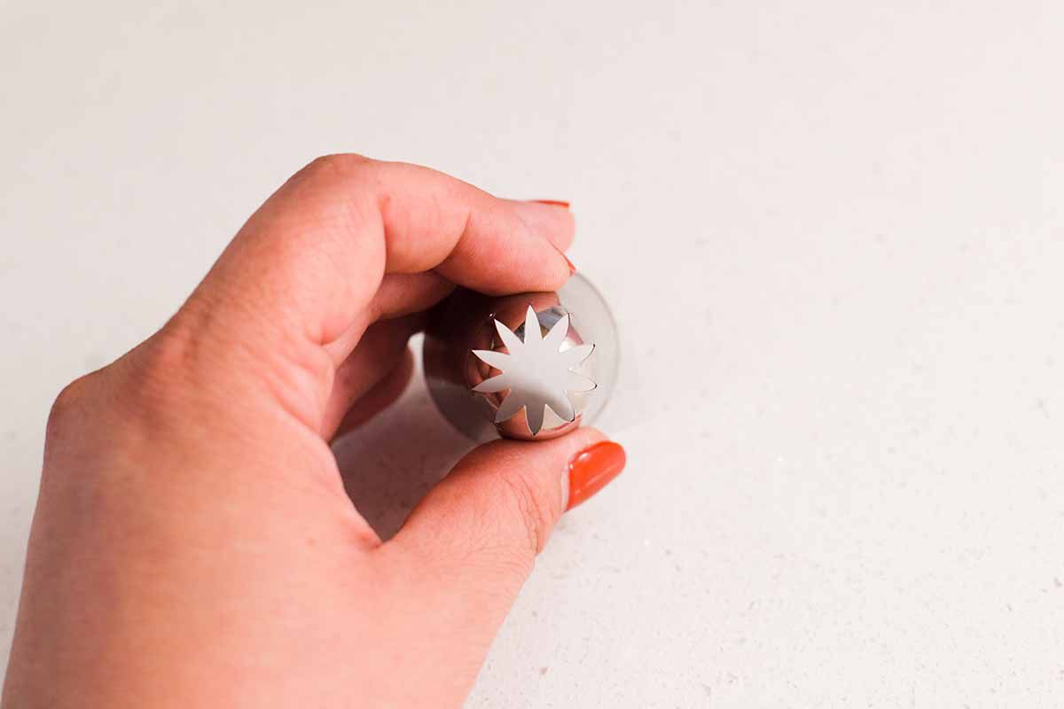 Woman with painted red fingernails holding a star piping tip.