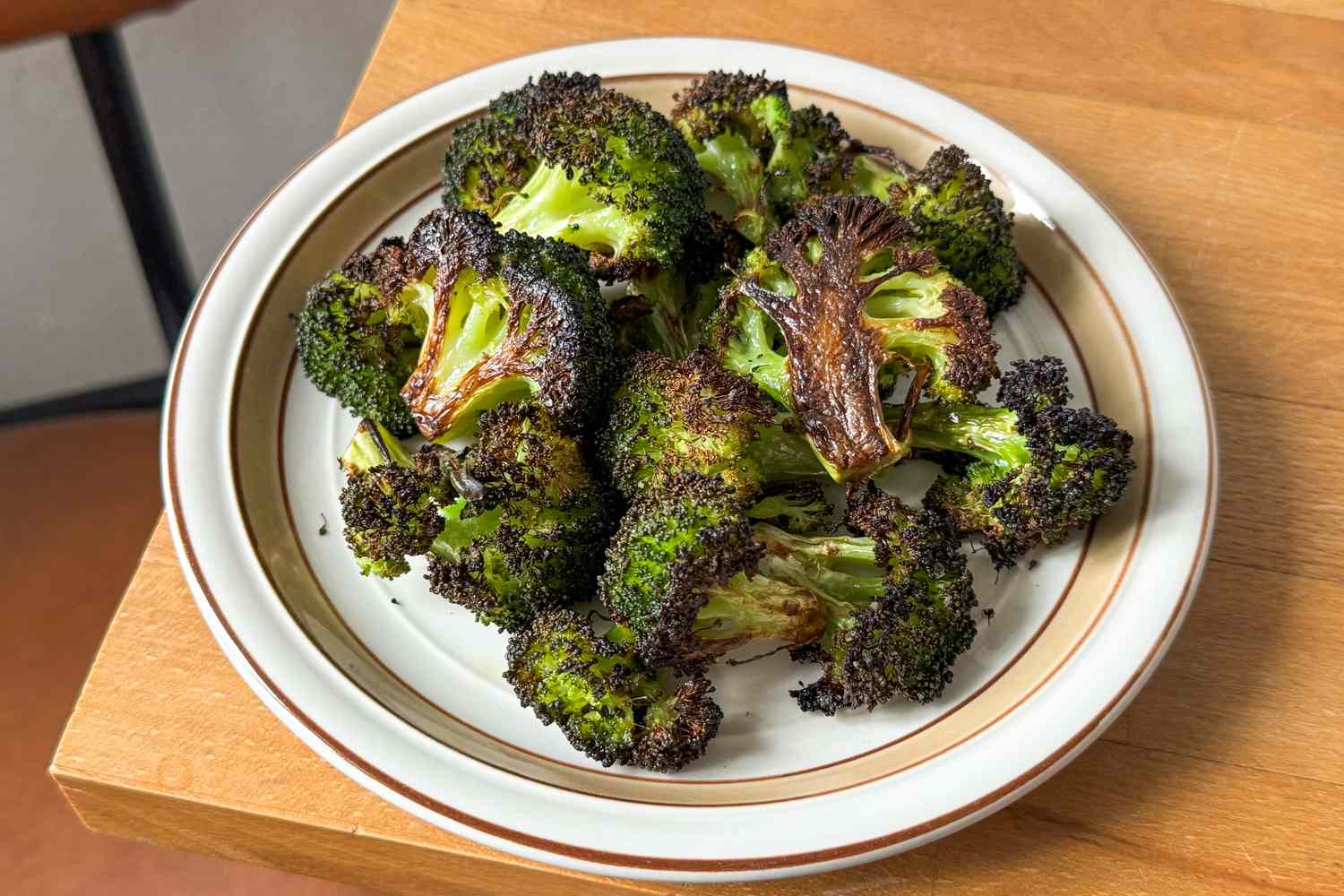 A plate of roasted broccoli florets arranged on a wooden table